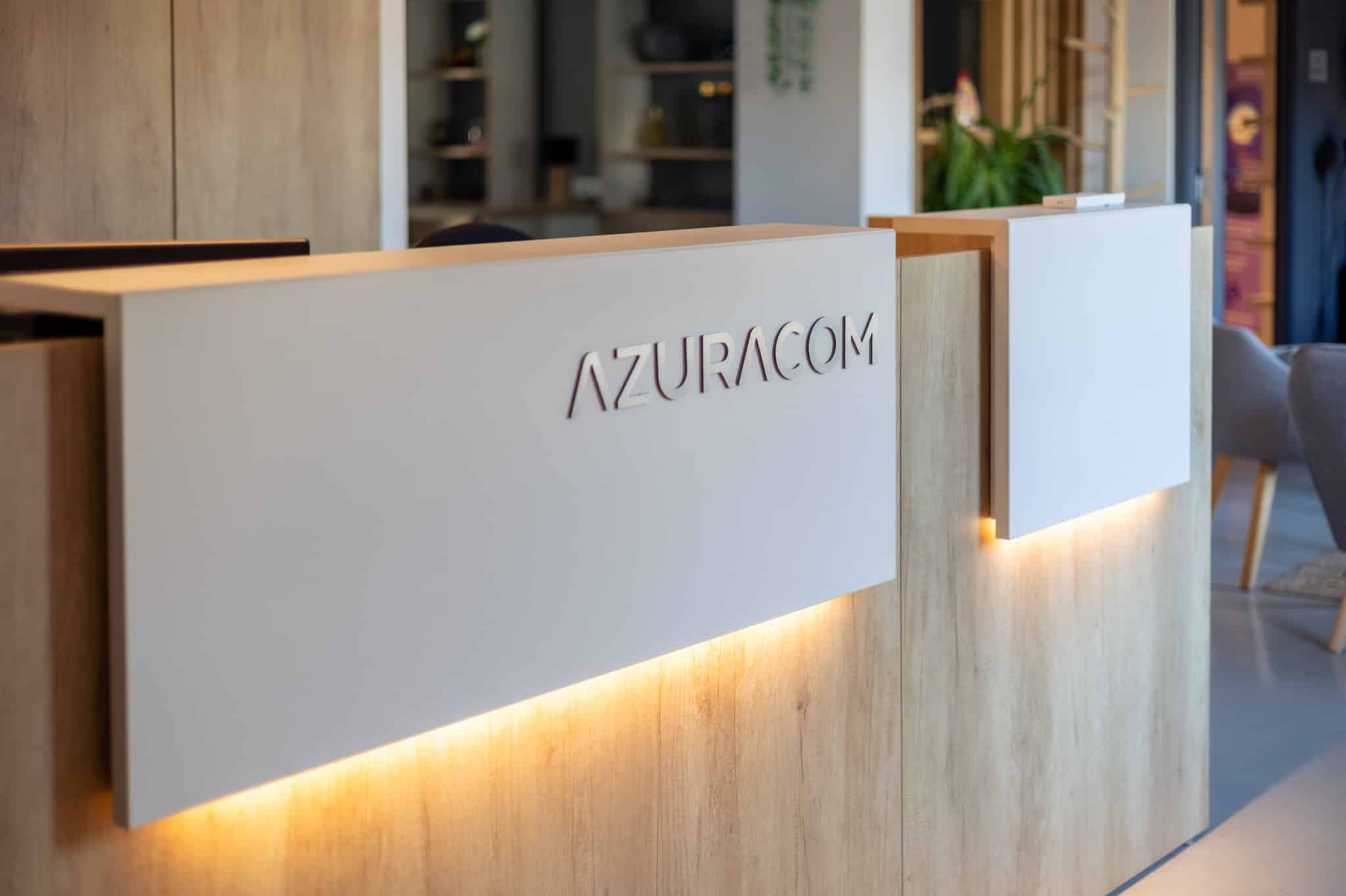 agence-web-azuracom-comptoir-accueil.jpg Comptoir d'accueil intérieur moderne des bureaux Azuracom. Un bureau et une zone de réception sont visibles.