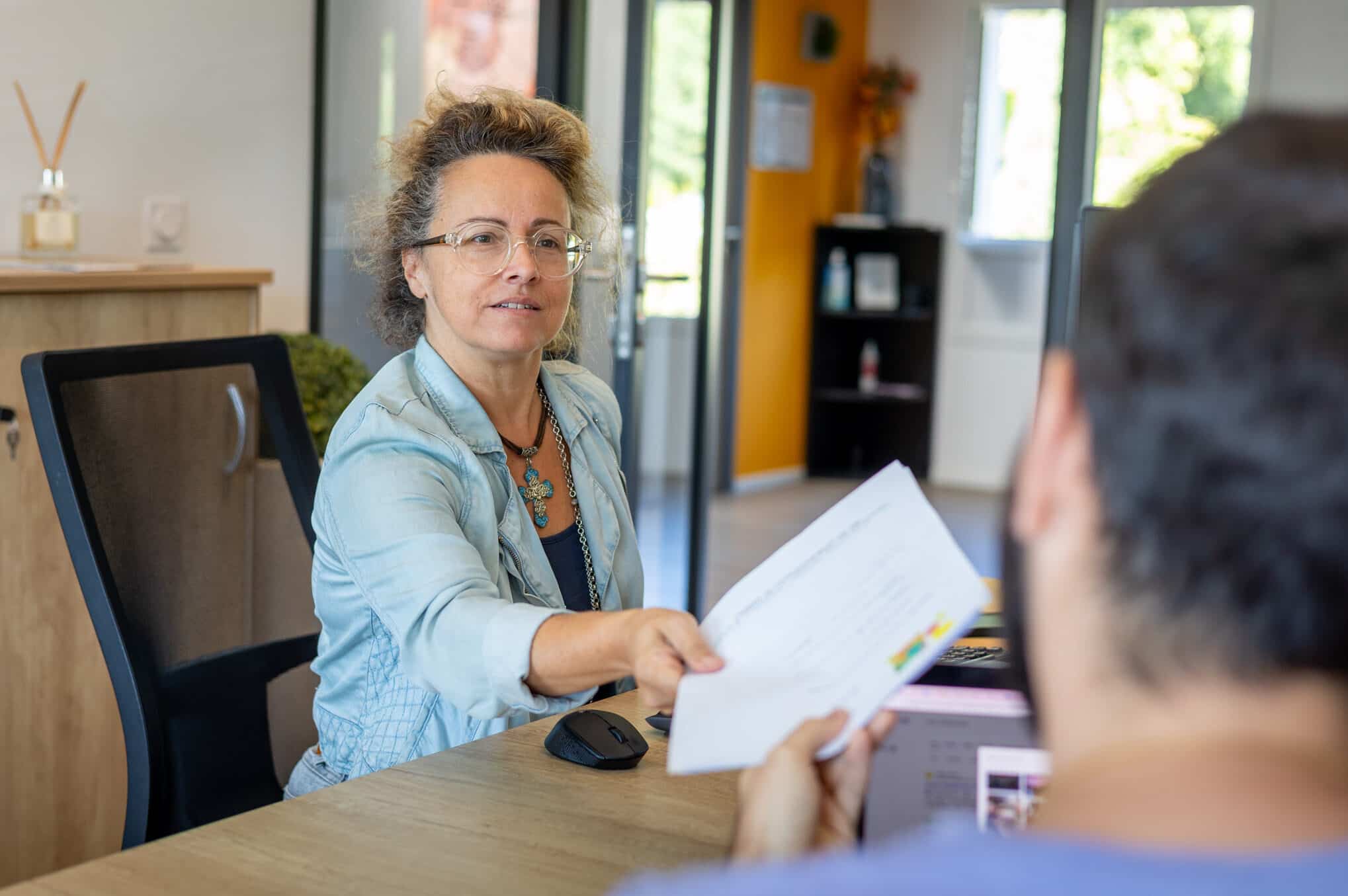 recrutement-dev Deux membres de l'équipe de l'agence web Azuracom discutent et échangent un dossier papier, symbolisant la collaboration et le partage d'informations en interne.