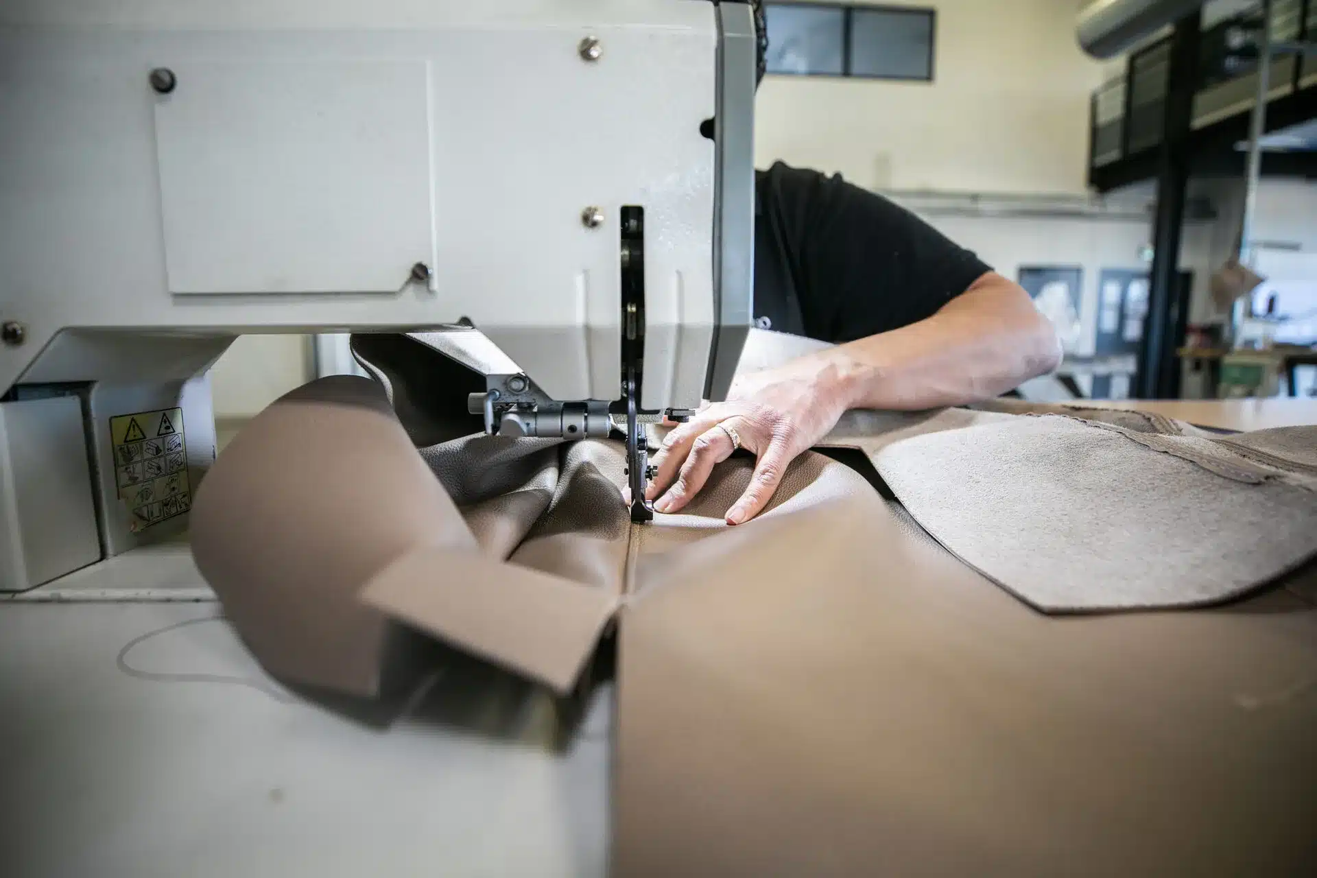 Artisan en train de coudre du cuir haut de gamme sur une machine industrielle, illustrant le savoir-faire mis en avant dans un site vitrine luxe.