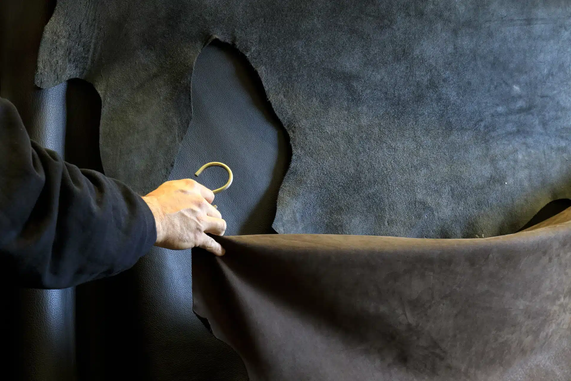 Main d’un artisan sélectionnant une peau haut de gamme dans un atelier, illustrant le choix des matériaux mis en avant sur un site vitrine luxe.