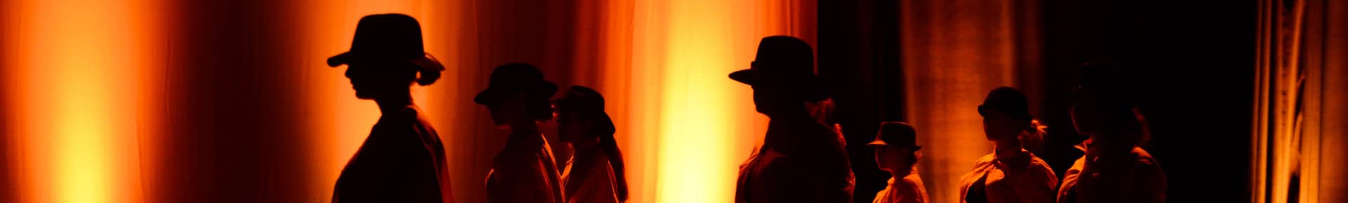 danseuses Silhouettes de danseurs portant des chapeaux, éclairées par une lumière orangée en arrière-plan, image issue du site web du Lieu Danse et utilisée pour illustrer un contenu lié au développement logiciel métier.