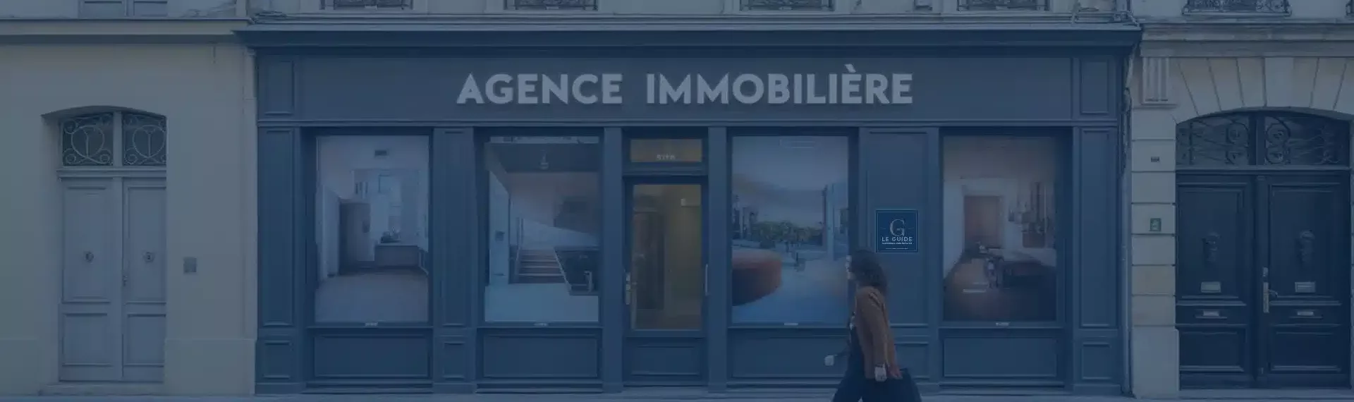 Une personne marche devant la vitrine d’une agence immobilière moderne affichant des visuels de biens, illustrant l’importance d’une création site immobilier sur mesure pour renforcer visibilité et image de marque.