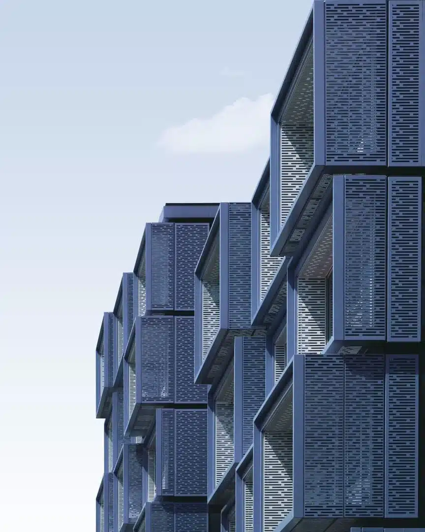 facade-architecturale-contemporaine Façade moderne d’un immeuble composée de modules géométriques en saillie, en métal bleu grisé avec motifs ajourés, éclairée par une lumière douce sous un ciel clair ; illustration utilisée dans un contexte lié à la création de plateforme de gestion d’adhérents