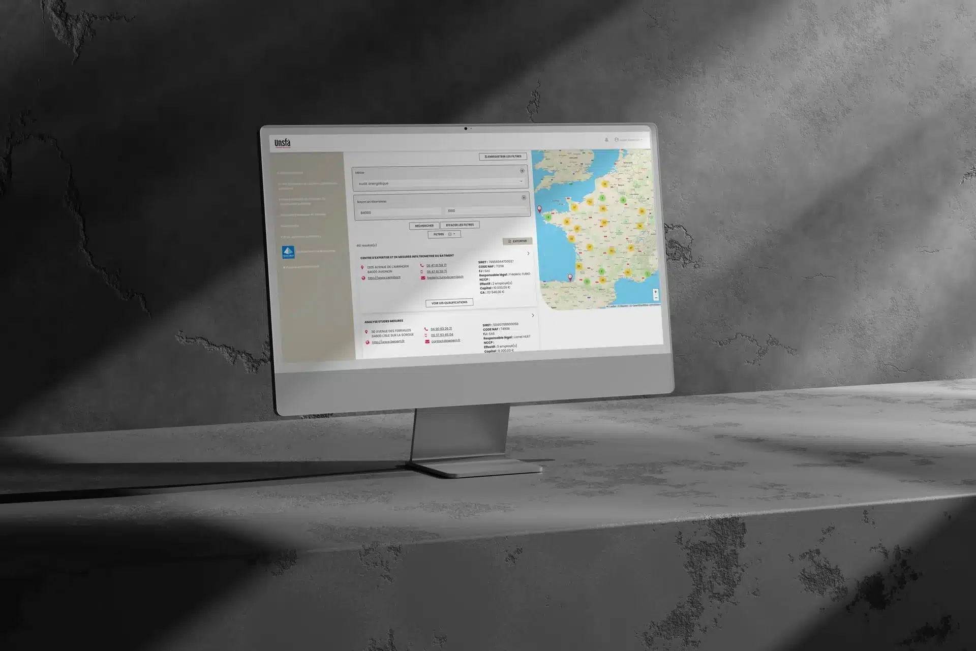 interface-recherche-UNSFA Écran d’ordinateur affichant une interface de recherche avancée avec carte interactive de la France, listes de résultats et filtres, posé sur une surface en béton éclairée par une lumière rasante ; illustration utilisée dans un contexte lié à la création de plateforme de gestion d’adhérents