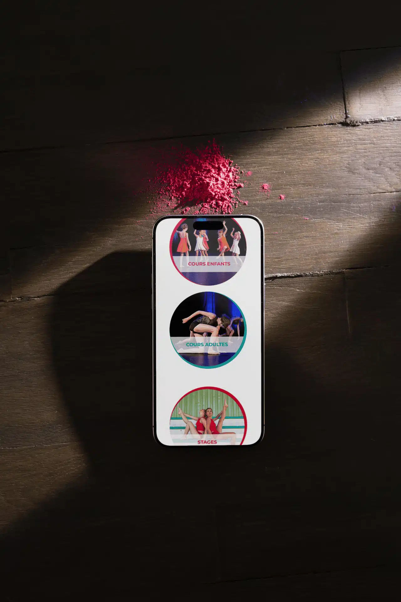 lieu-danse-smartphone Smartphone affichant les pages « Cours enfants », « Cours adultes » et « Stages » du site du Lieu Danse, posé sur un sol en bois avec de la poudre rose, utilisé dans un contenu lié au développement logiciel métier.