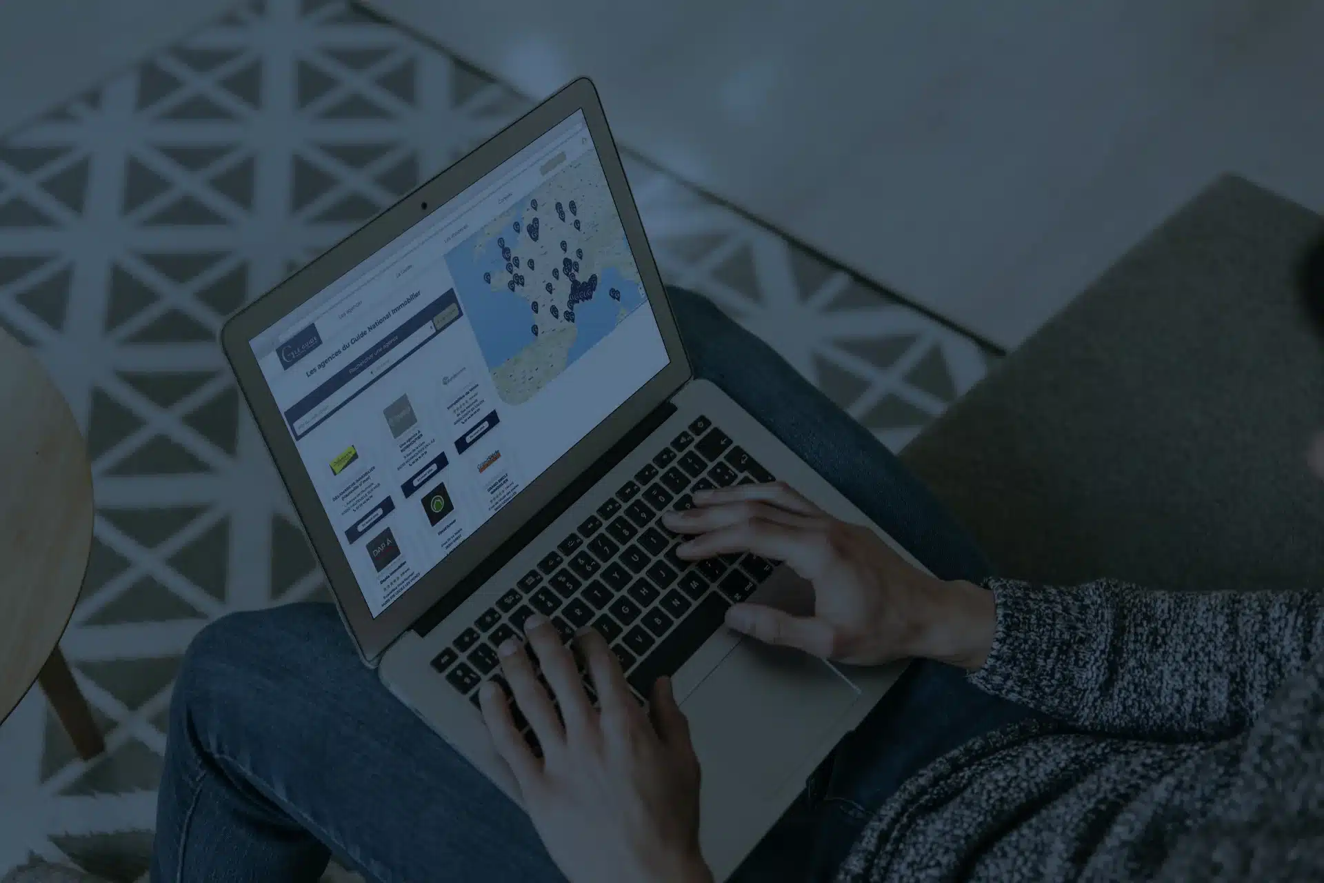 Une personne consulte sur un ordinateur portable une plateforme immobilière affichant une carte interactive et des services en ligne, illustrant l’efficacité d’une création site immobilier sur mesure orientée utilisateur.