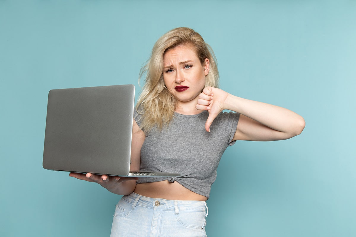 Femme tenant un ordinateur portable avec un geste négatif, illustrant un site obsolète ou une expérience utilisateur décevante en ligne.